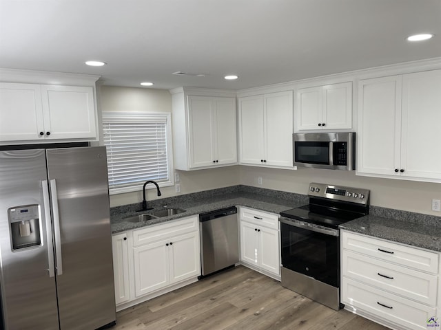 kitchen featuring light hardwood / wood-style floors, appliances with stainless steel finishes, dark stone countertops, white cabinets, and sink