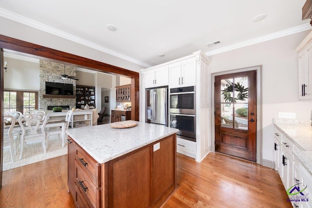 kitchen with white cabinetry, light wood-type flooring, appliances with stainless steel finishes, a kitchen island, and light stone countertops