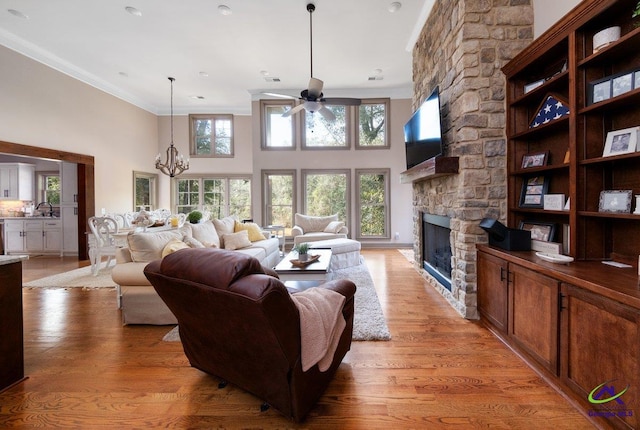 living room with sink, a fireplace, ornamental molding, light hardwood / wood-style floors, and ceiling fan with notable chandelier