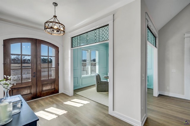 entryway with vaulted ceiling, a chandelier, wood-type flooring, and french doors