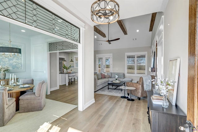 living room with beam ceiling, a high ceiling, ceiling fan with notable chandelier, and light hardwood / wood-style flooring