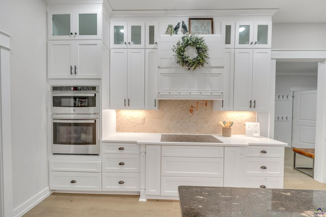 kitchen featuring tasteful backsplash, dark stone countertops, white cabinetry, stainless steel double oven, and black electric cooktop