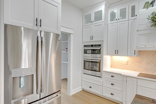 kitchen featuring exhaust hood, white cabinetry, light hardwood / wood-style floors, appliances with stainless steel finishes, and backsplash