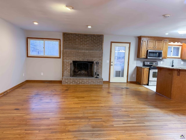 kitchen with appliances with stainless steel finishes, light hardwood / wood-style floors, sink, backsplash, and a brick fireplace