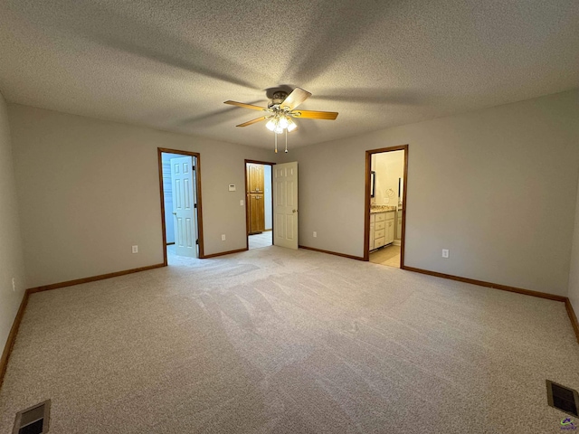 unfurnished bedroom with ceiling fan, ensuite bath, a closet, light colored carpet, and a textured ceiling