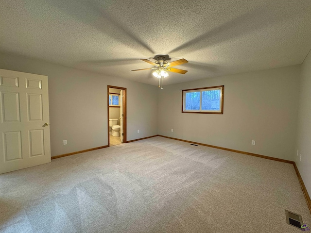 unfurnished bedroom with ceiling fan, connected bathroom, light carpet, and a textured ceiling