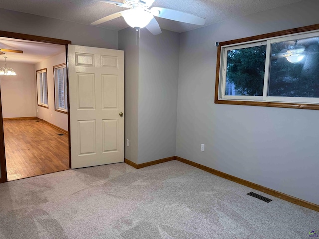 carpeted spare room with a textured ceiling and ceiling fan with notable chandelier