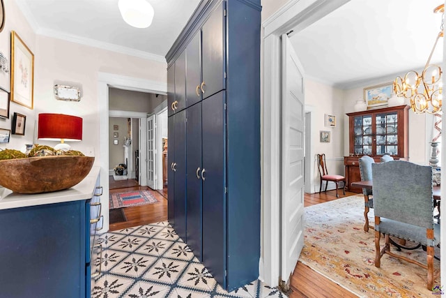 hall with light wood-type flooring, ornamental molding, and a notable chandelier