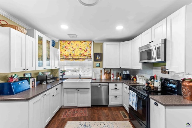 kitchen with appliances with stainless steel finishes, backsplash, dark hardwood / wood-style flooring, white cabinets, and sink