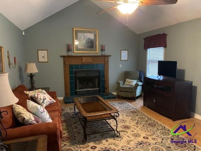 living room with lofted ceiling, ceiling fan, a tile fireplace, and light hardwood / wood-style flooring