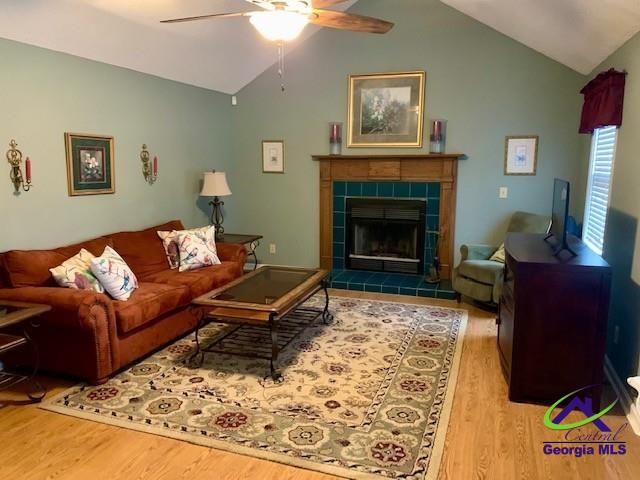 living room with ceiling fan, vaulted ceiling, a fireplace, and hardwood / wood-style flooring