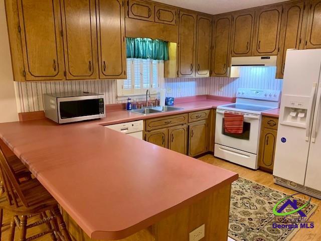 kitchen featuring kitchen peninsula, sink, white appliances, and a breakfast bar area