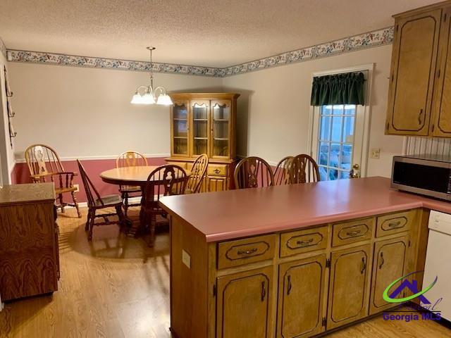 kitchen featuring a textured ceiling, decorative light fixtures, an inviting chandelier, light wood-type flooring, and white dishwasher