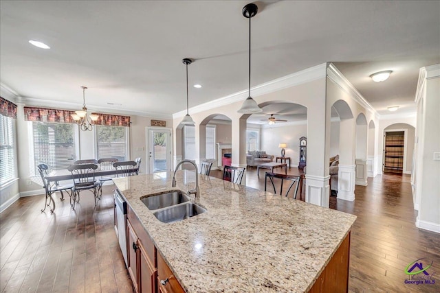 kitchen with light stone countertops, an island with sink, sink, hanging light fixtures, and stainless steel dishwasher