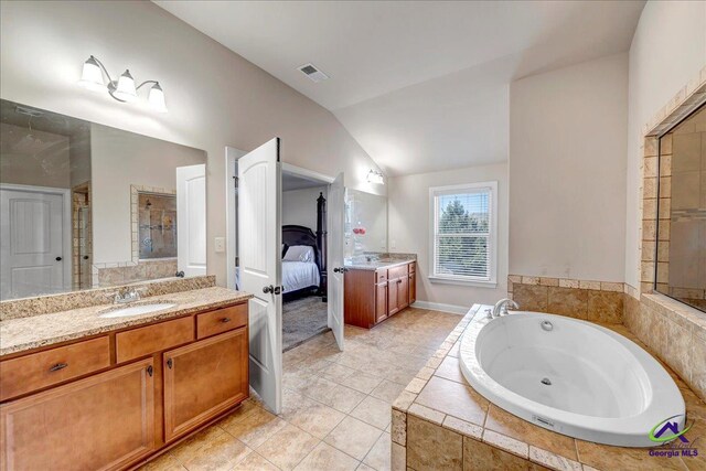 bathroom with tile patterned flooring, vanity, vaulted ceiling, and a relaxing tiled tub