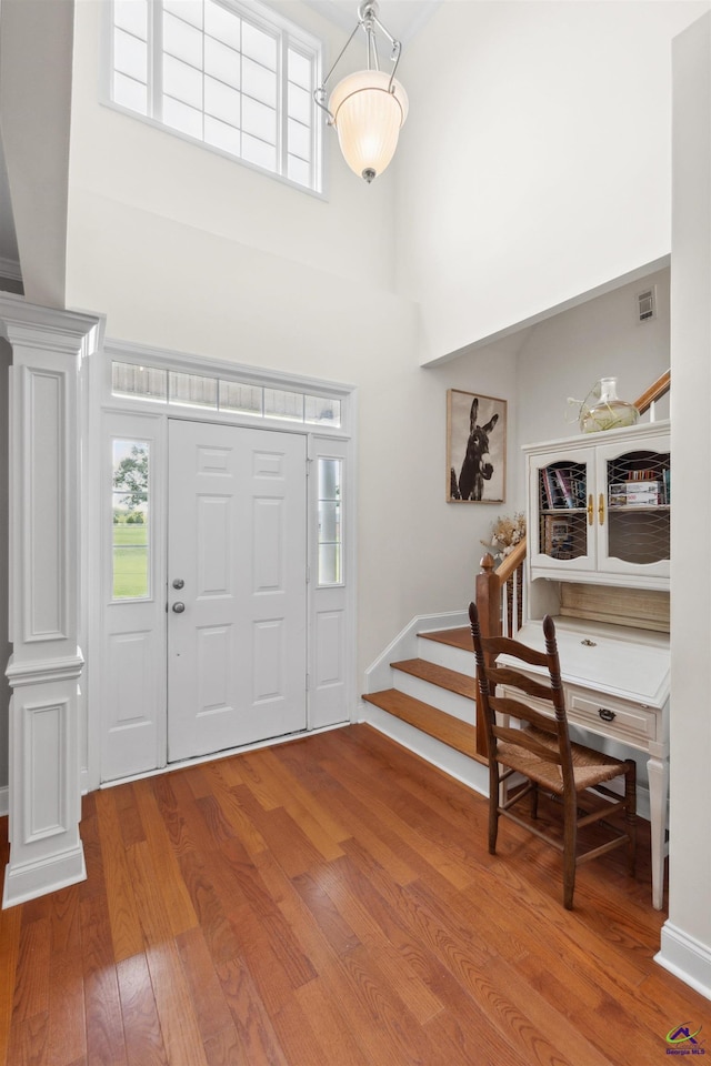 entrance foyer with decorative columns, a high ceiling, and wood-type flooring