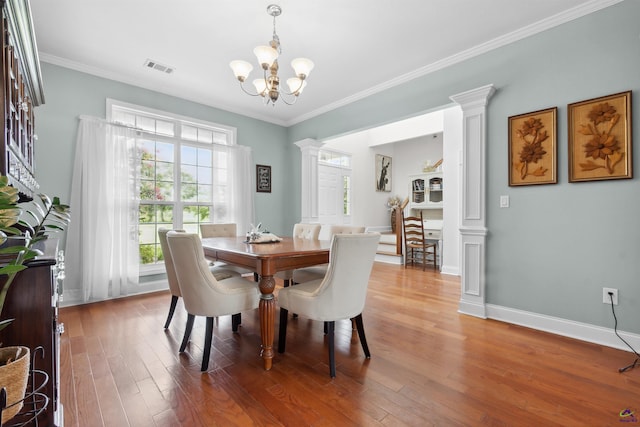 dining space with decorative columns, hardwood / wood-style floors, ornamental molding, and a chandelier