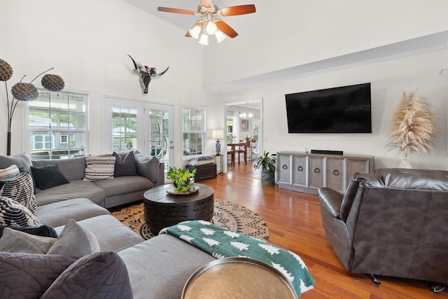 living room featuring light hardwood / wood-style floors, ceiling fan with notable chandelier, and a towering ceiling