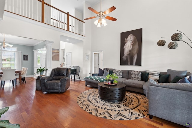 living room with decorative columns, hardwood / wood-style flooring, ceiling fan with notable chandelier, and a towering ceiling