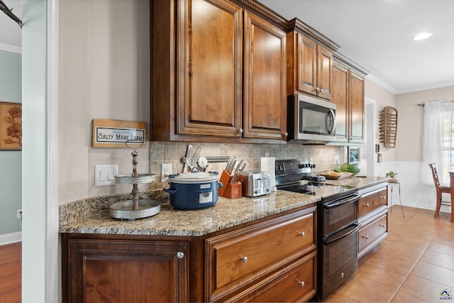 kitchen featuring light stone counters, light tile patterned flooring, range with two ovens, ornamental molding, and decorative backsplash