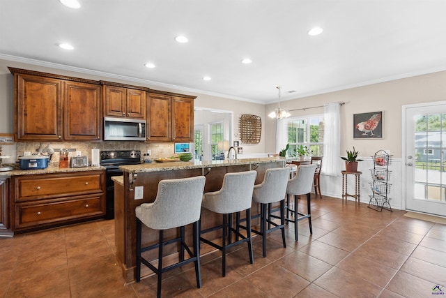 kitchen featuring double oven range, hanging light fixtures, a center island with sink, and crown molding