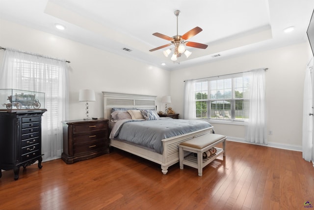 bedroom with wood-type flooring, ceiling fan, and a raised ceiling