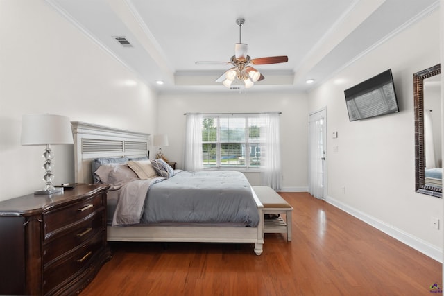 bedroom with ceiling fan, hardwood / wood-style floors, crown molding, and a raised ceiling