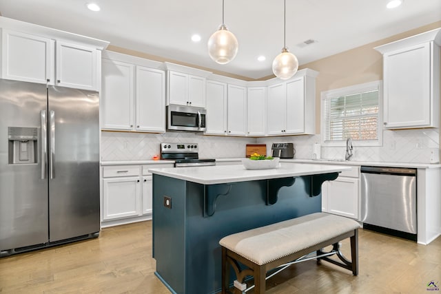 kitchen with light hardwood / wood-style flooring, decorative light fixtures, white cabinets, a center island, and stainless steel appliances