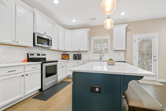 kitchen with white cabinets, decorative light fixtures, appliances with stainless steel finishes, and light wood-type flooring