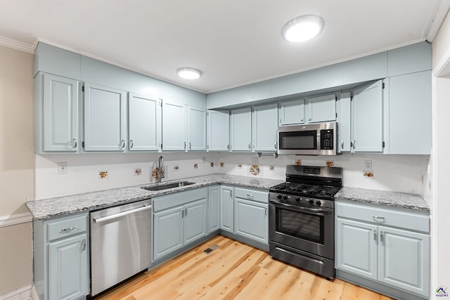 kitchen featuring light stone countertops, light hardwood / wood-style floors, sink, ornamental molding, and stainless steel appliances