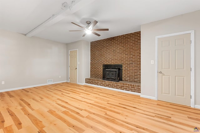 unfurnished living room with a wood stove, beamed ceiling, ceiling fan, and hardwood / wood-style flooring