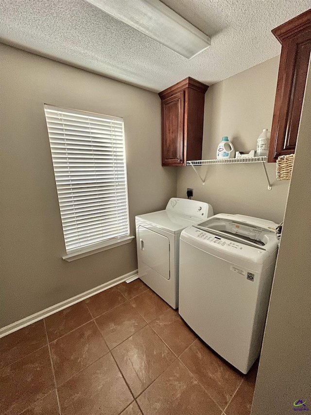 washroom featuring dark tile patterned flooring, cabinets, a textured ceiling, and washer and clothes dryer