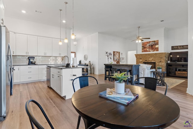 dining space with sink, crown molding, ceiling fan, a fireplace, and light hardwood / wood-style floors