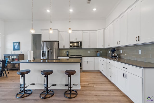 kitchen featuring white cabinetry, a kitchen island with sink, a breakfast bar, and appliances with stainless steel finishes