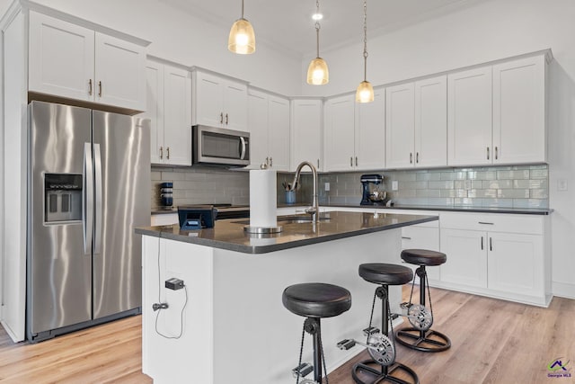 kitchen featuring a kitchen island with sink, backsplash, white cabinets, and appliances with stainless steel finishes