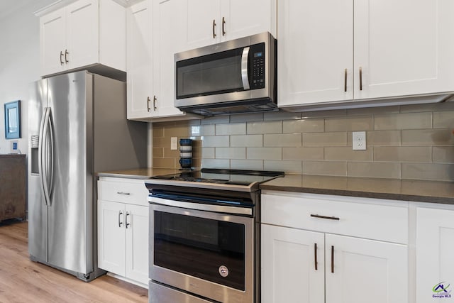 kitchen featuring white cabinetry, stainless steel appliances, tasteful backsplash, dark stone counters, and light wood-type flooring