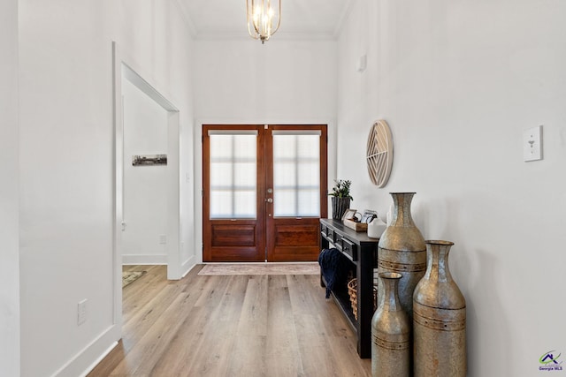 entrance foyer with french doors, crown molding, an inviting chandelier, and light hardwood / wood-style flooring