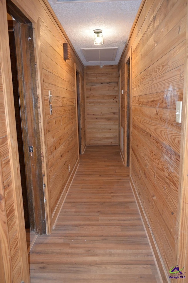 hall featuring hardwood / wood-style flooring, wooden walls, and a textured ceiling