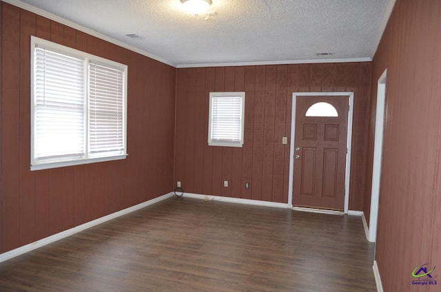 foyer featuring crown molding, a wealth of natural light, wooden walls, and dark wood-type flooring