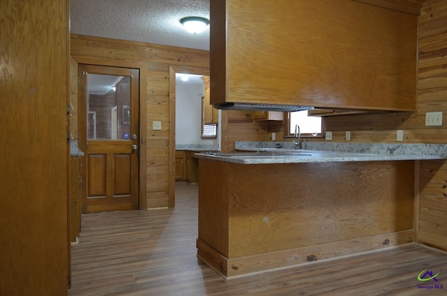 kitchen featuring kitchen peninsula, a textured ceiling, wooden walls, and light hardwood / wood-style flooring