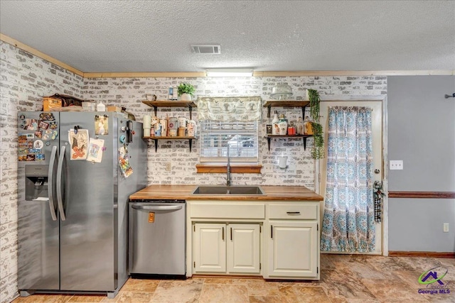 kitchen featuring brick wall, appliances with stainless steel finishes, sink, and butcher block countertops