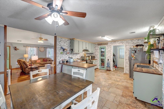 kitchen featuring sink, refrigerator, a textured ceiling, brick wall, and wood counters