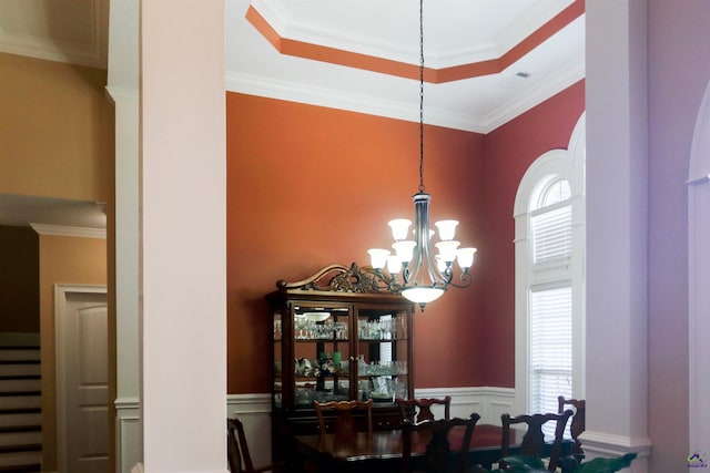 dining room with an inviting chandelier, ornamental molding, a raised ceiling, and a high ceiling