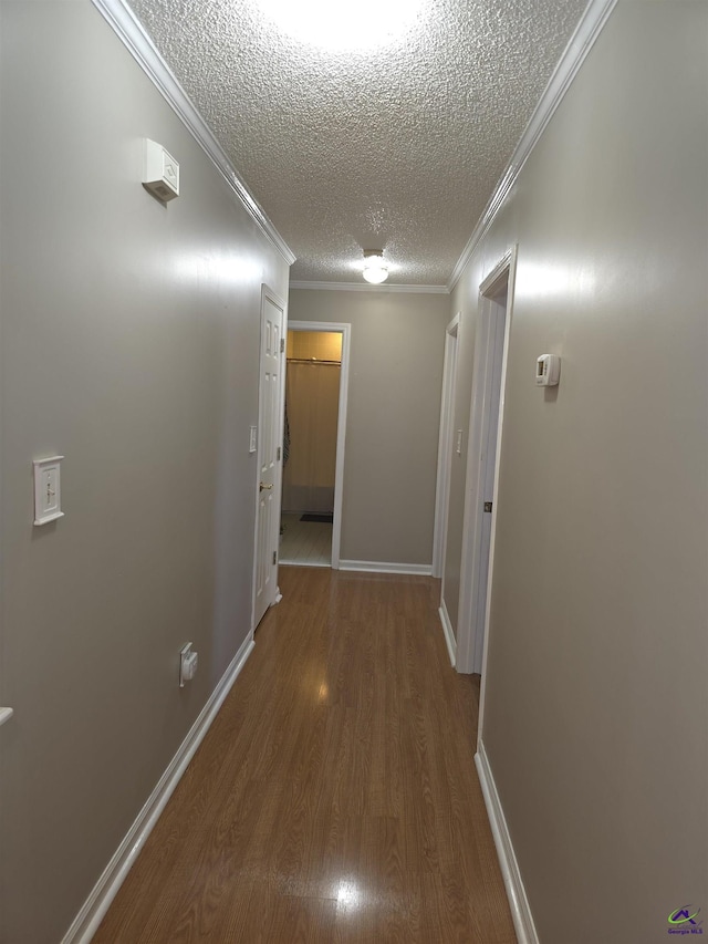 hallway with a textured ceiling, baseboards, wood finished floors, and crown molding