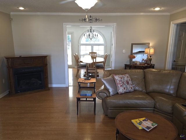 living area featuring baseboards, wood finished floors, crown molding, a fireplace, and a notable chandelier