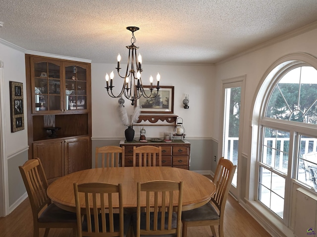 dining space with a textured ceiling, crown molding, wood finished floors, and an inviting chandelier