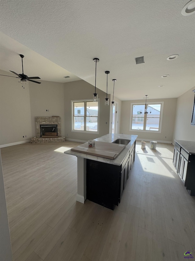 kitchen with a brick fireplace, a kitchen island, light wood-type flooring, and decorative light fixtures