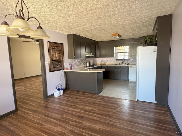 kitchen with dark wood-type flooring, white appliances, kitchen peninsula, and sink