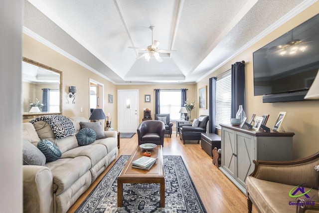 living room featuring crown molding, ceiling fan, a textured ceiling, a raised ceiling, and light wood-type flooring