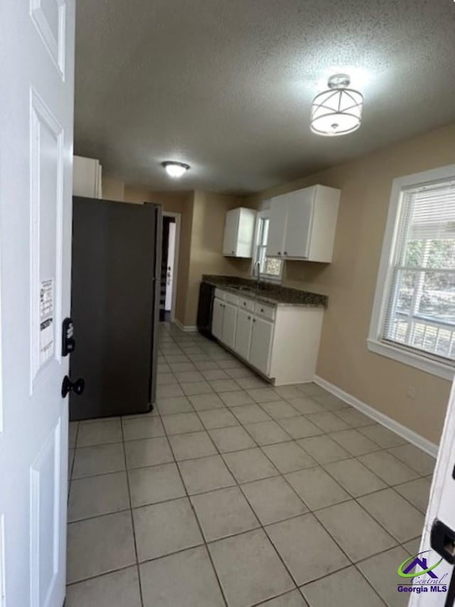 kitchen with white cabinetry, black refrigerator, light tile patterned flooring, and a textured ceiling